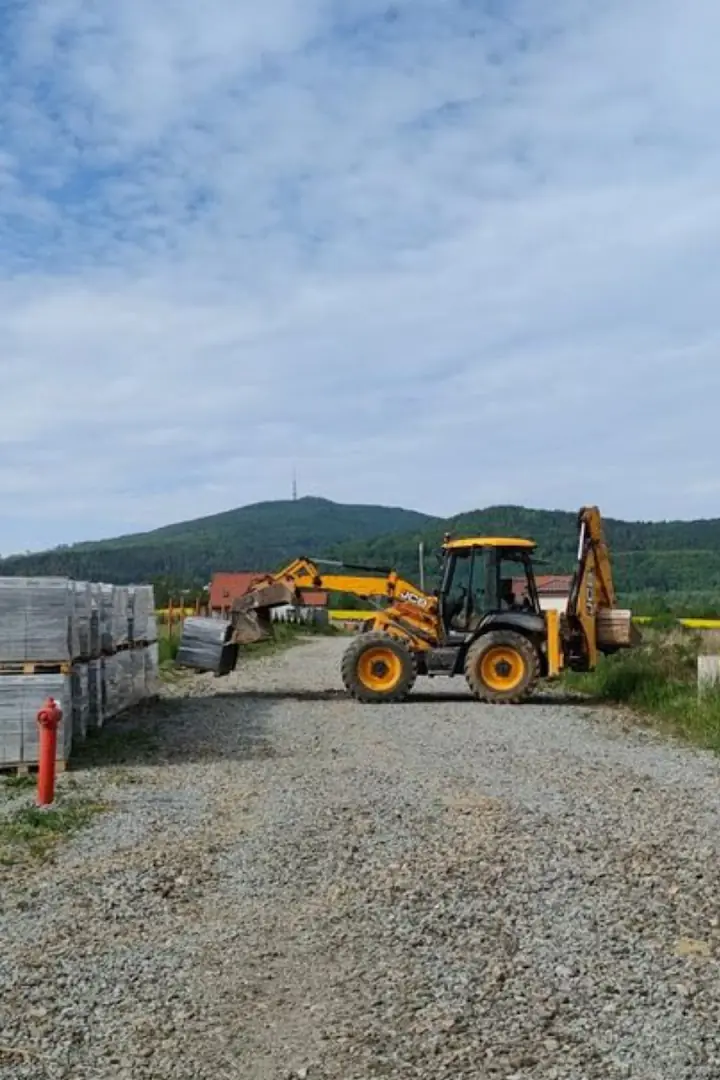 Koparko-ładowarka JCB na placu budowy, w tle góry